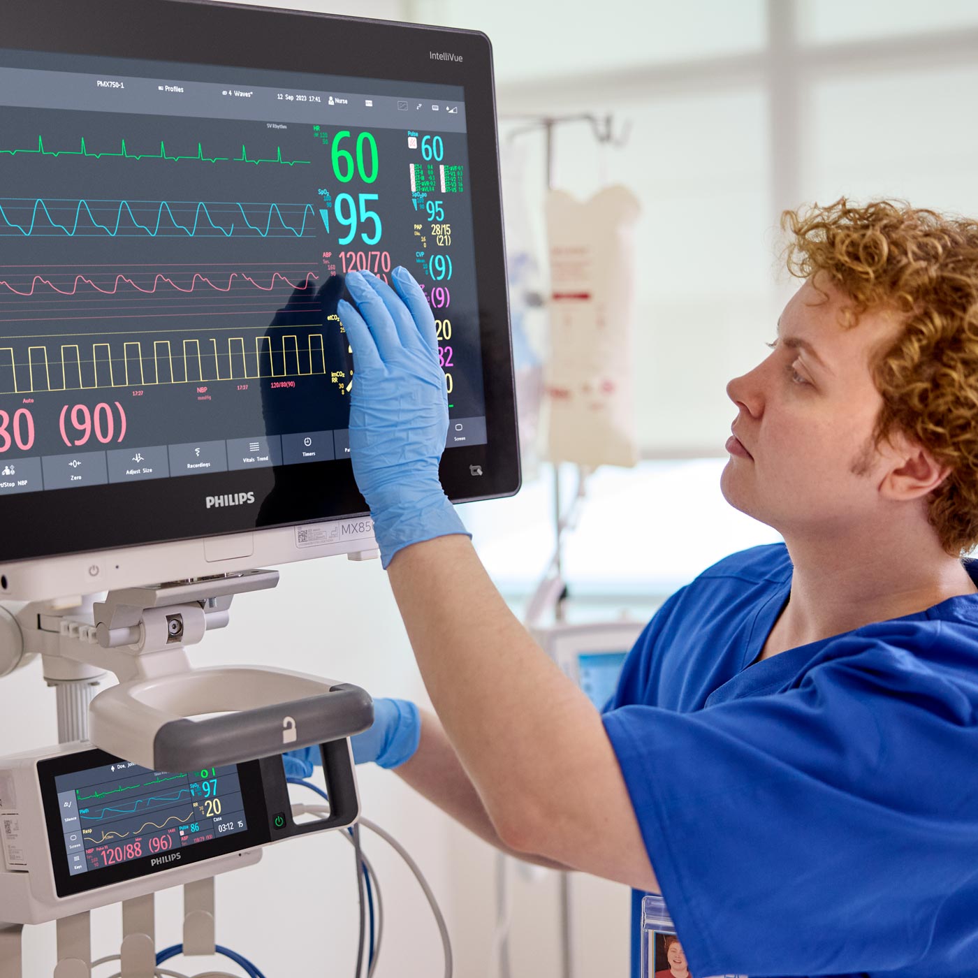 Healthcare provider touches monitor at an ICU bedside